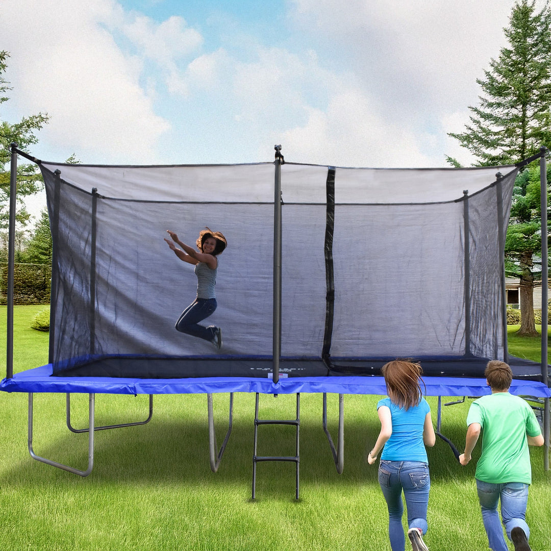 A girl jumps on a blue trampoline with a safety net in a backyard. Two kids run towards it. The sky is partly cloudy, and there are trees in the background.