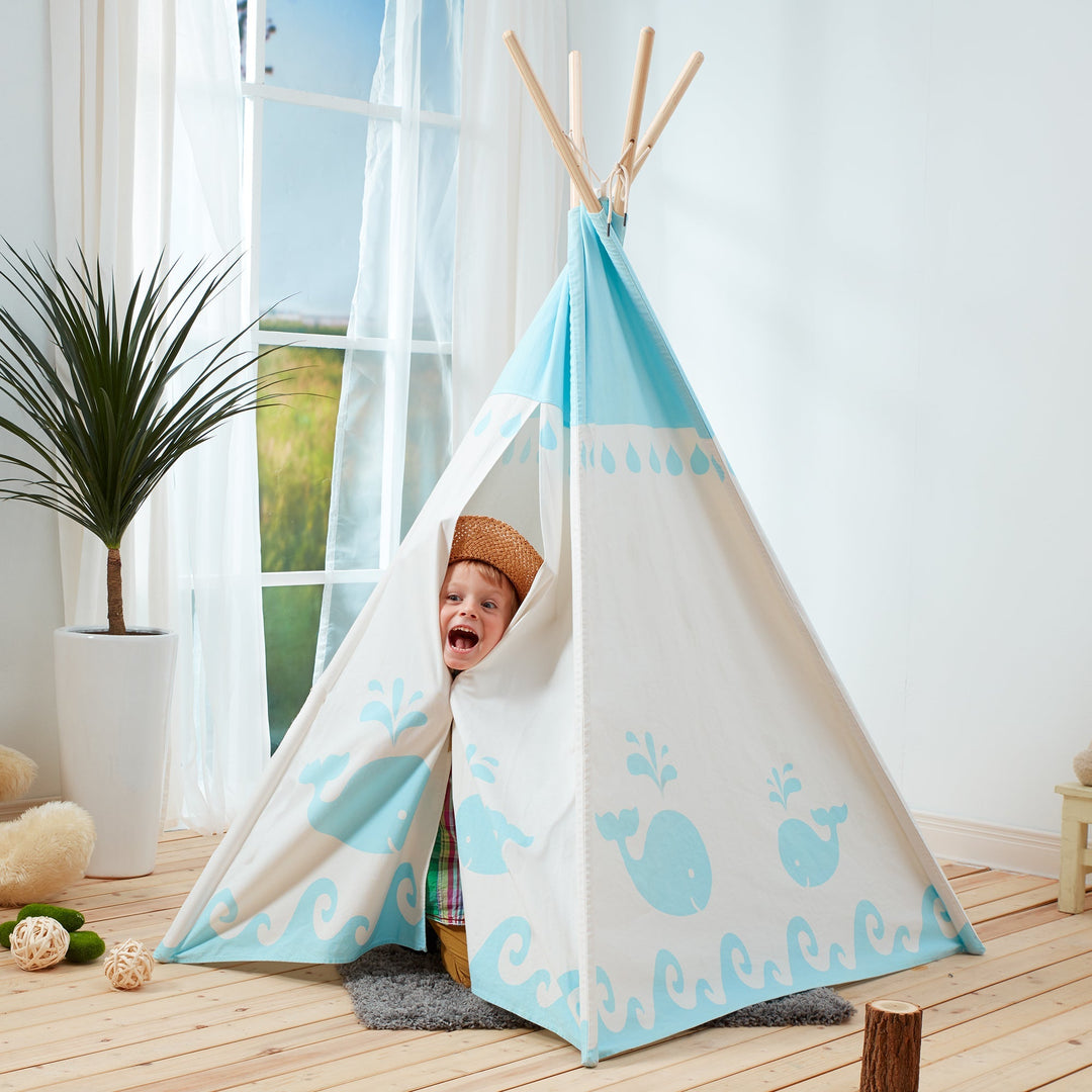 A little boy peeking out of a white with blue whales indoor teepee play tent