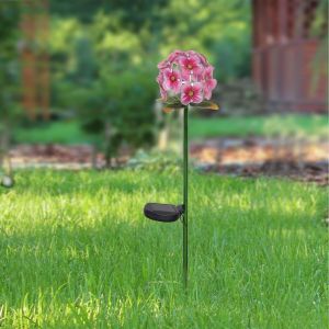 A garden stake with pink flowers on top and a solar light in the middle stands in a yard.