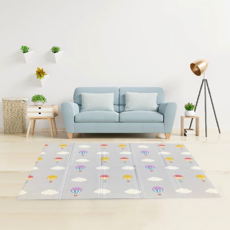 A kids playmat with hot air balloons and clouds is on the floor by a blue couch.