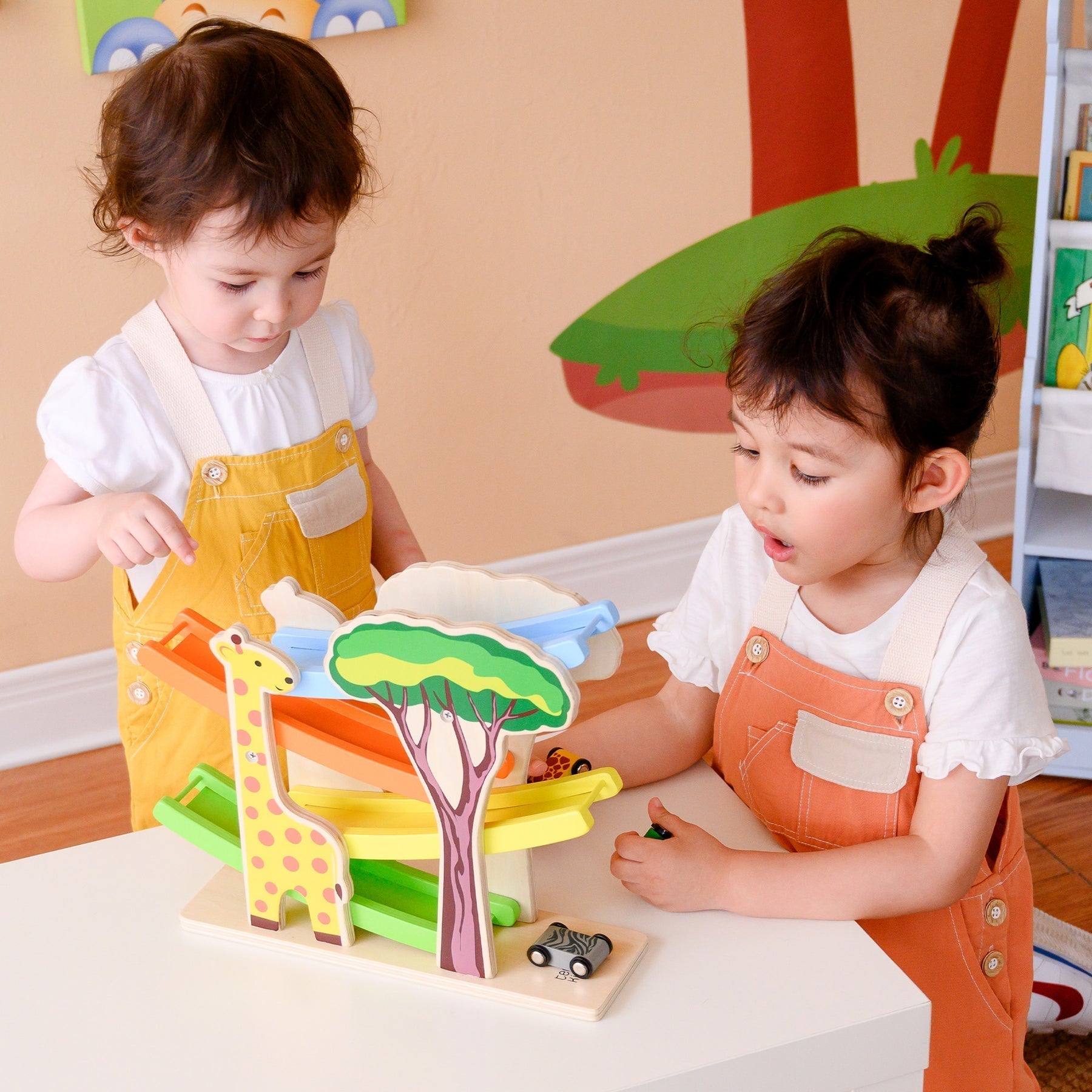 Two young kids playing with a teamson kids toys that features colorful slides and a giraffe.