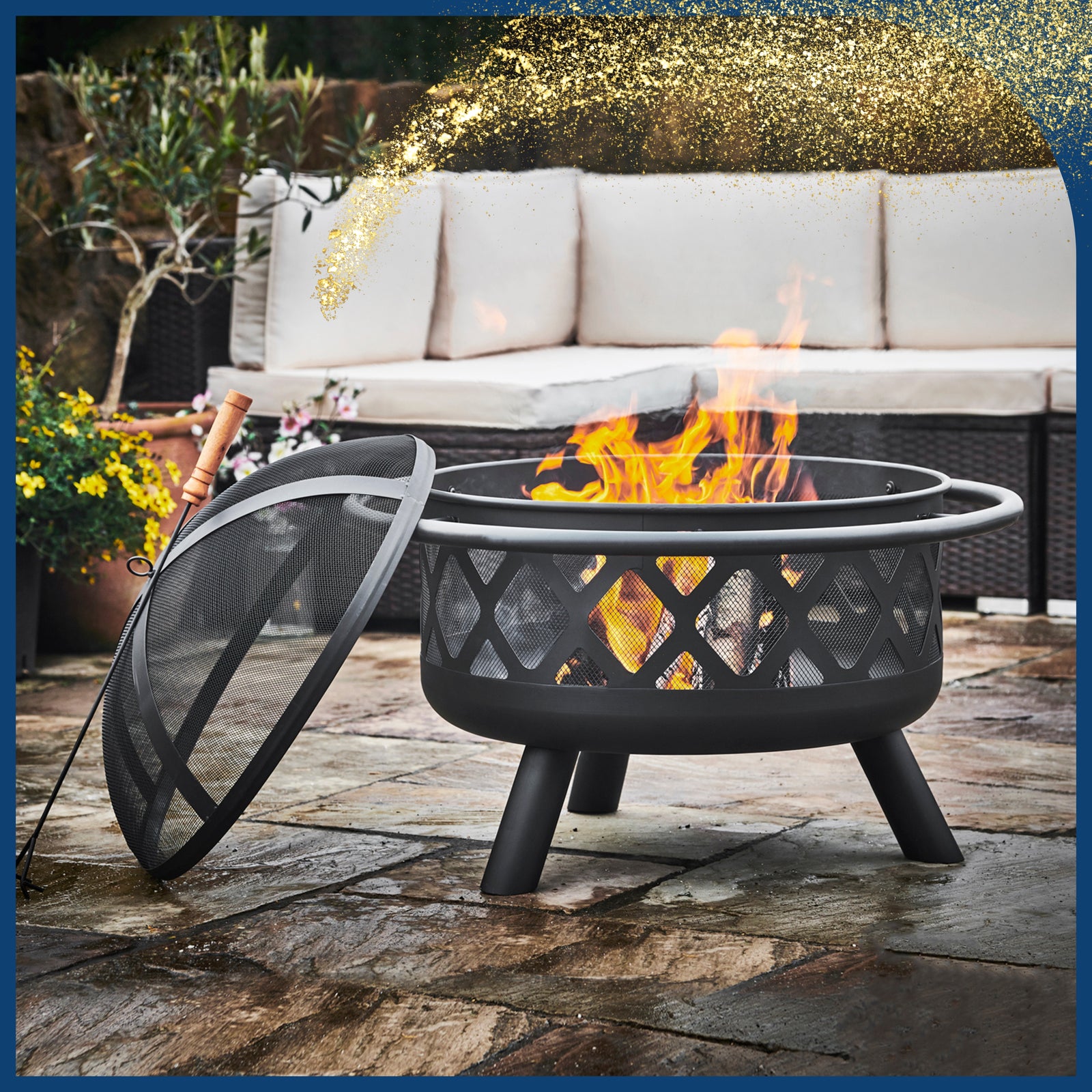 a black decorative fire pit holds a fire next to an outdoor couch on a chilly fall day