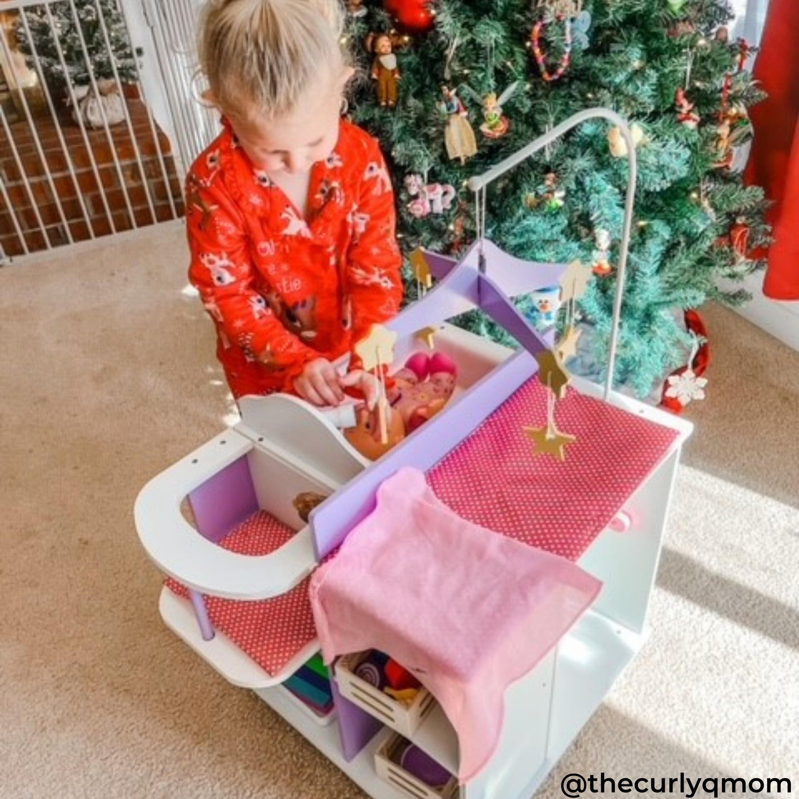 A girl playing with the doll nursery station next to a Christmas tree