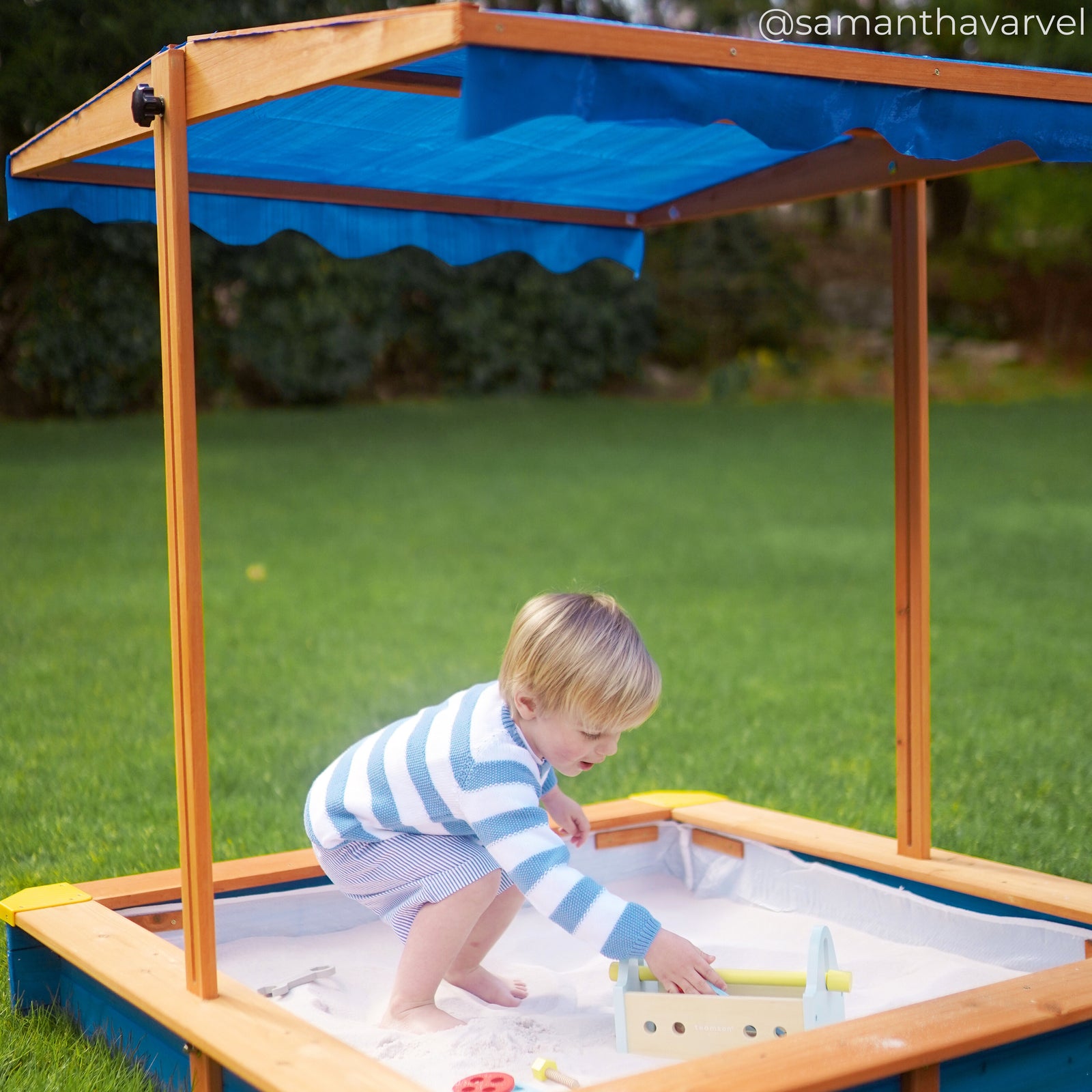 a young boy plays in his large sand box, protected from the sun with the canopy overhead