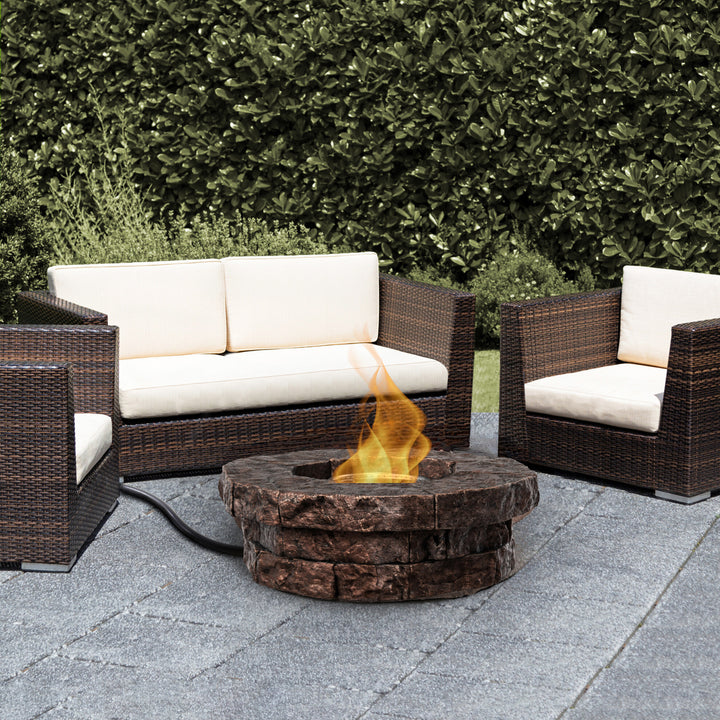 A round faux brick gas fire pit surrounded by brown PE rattan furniture outside