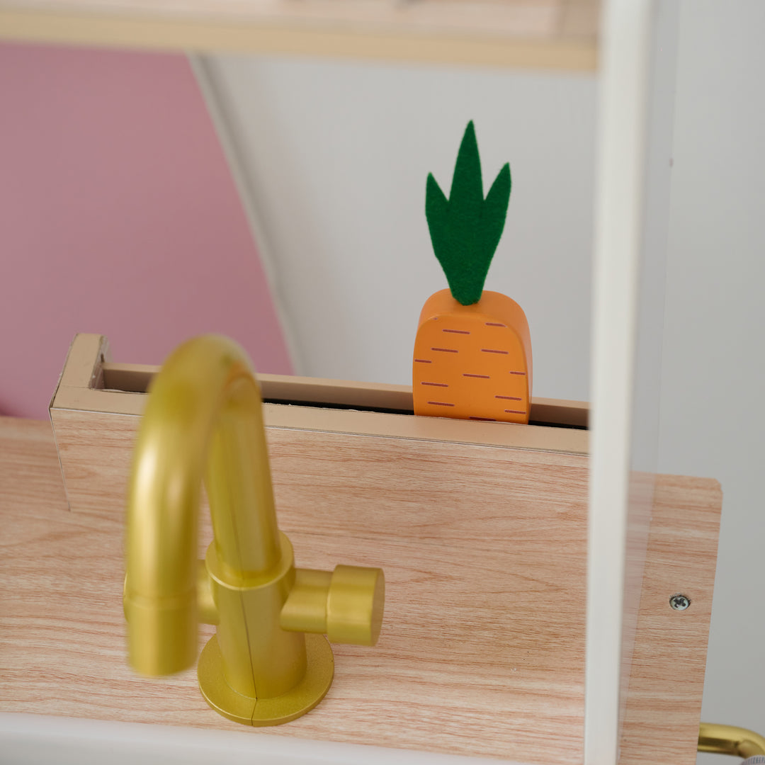 Close-up of gold toy faucet and wooden mini garden with a wooden carrot in a kids play kitchen set.