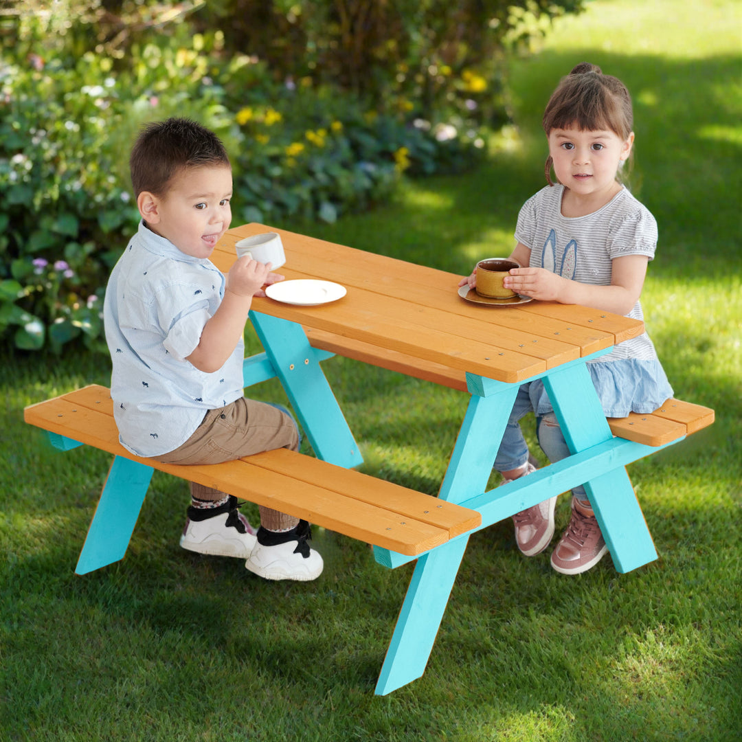 Two kids drinking and sitting on Teamson Kids Child Sized Wooden Outdoor Picnic Table benches