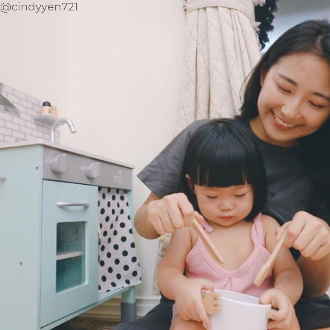 A mom and little girl stiring pretend food next to a play kitchen