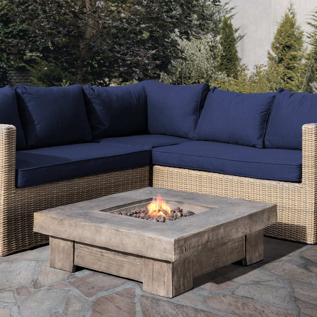 A square-shape gas fire pit infront of an outdoor seating area with blue cushions