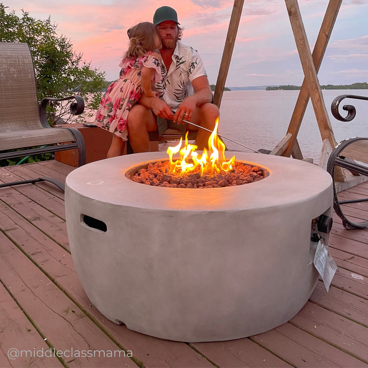A father and daughter sitting next to a faux concrete round gas fire pit