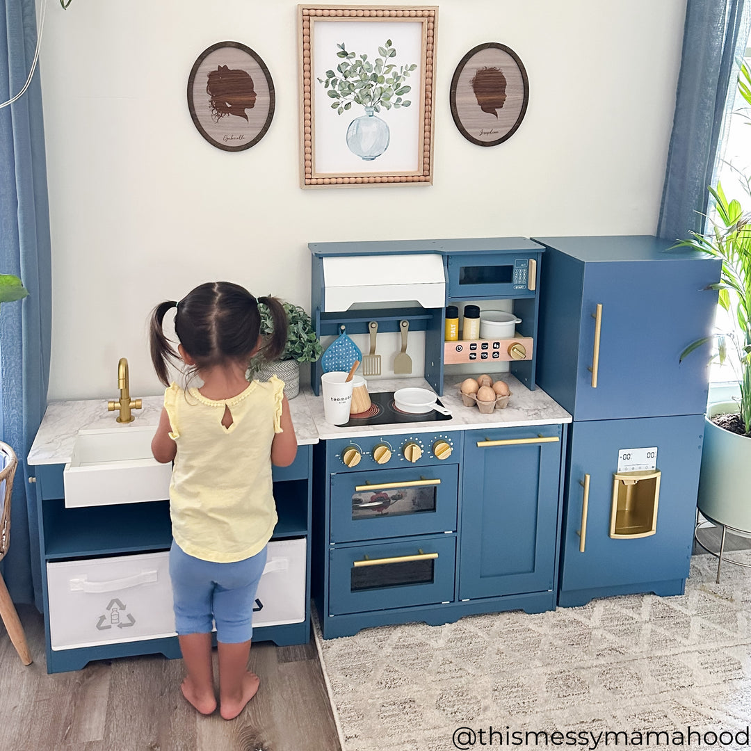 A little girl standing at the sink of her play kitchen 