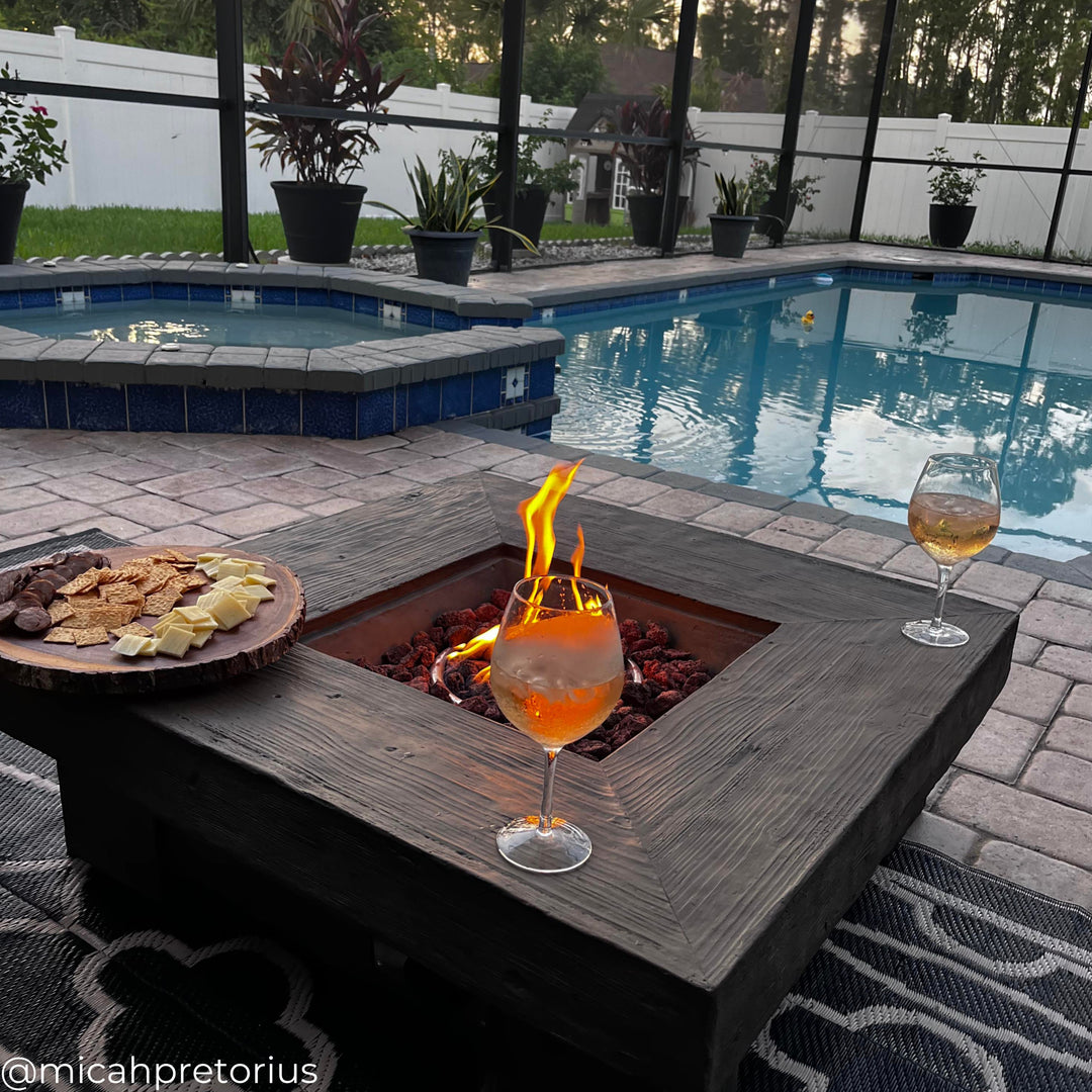 A square-shape gas fire pit with a fire next to a swimming pool