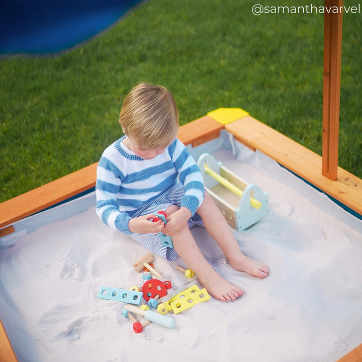A little boy sitting in a sandbox playing with tools
