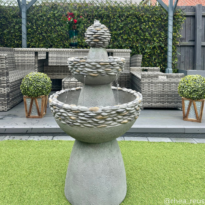 3-tiered birdbath style water fountain with pebble accents in front of a patio