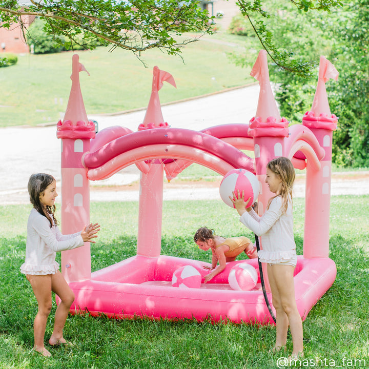 A pair of girls tossing a beach ball back and forth while a younger girl reaches into the sprinkler castle