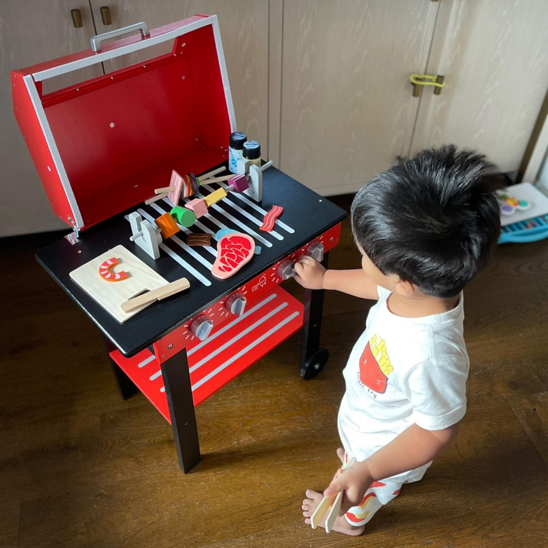 A little boy playing with a pretend BBQ grill with pretend food and condiments