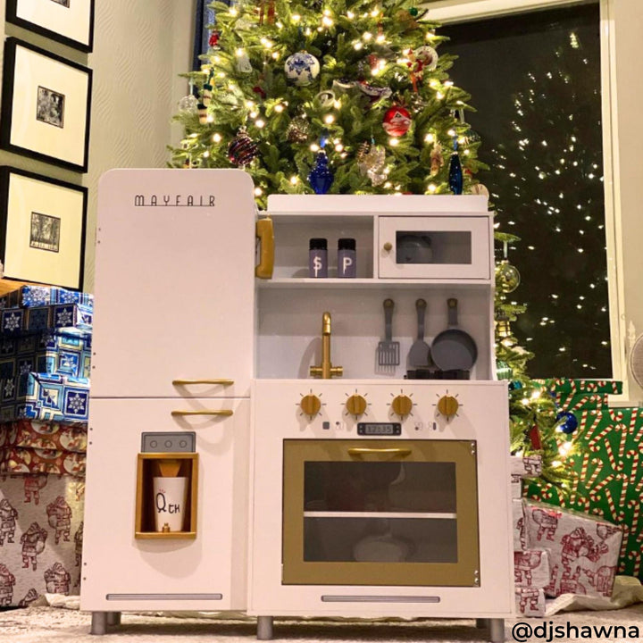 A white and gold retro-styled play kitchen in front of a Christmas tree