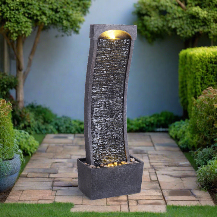 A waterfall fountain, charcoal, with LED lights illuminated at the top and bottom, on a patio.