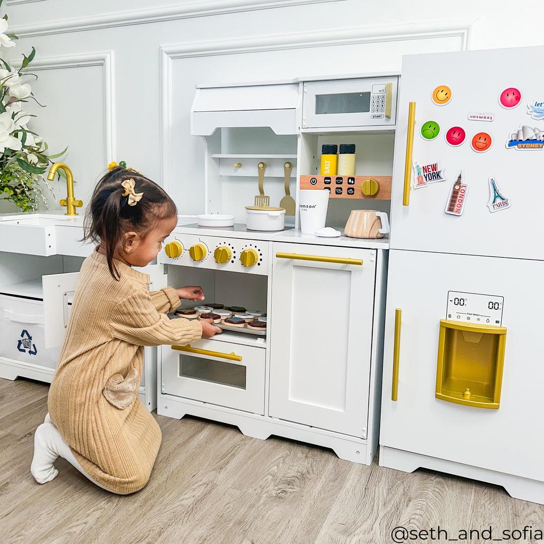 A little girl putting a tray of play food in the oven of her play kitchen