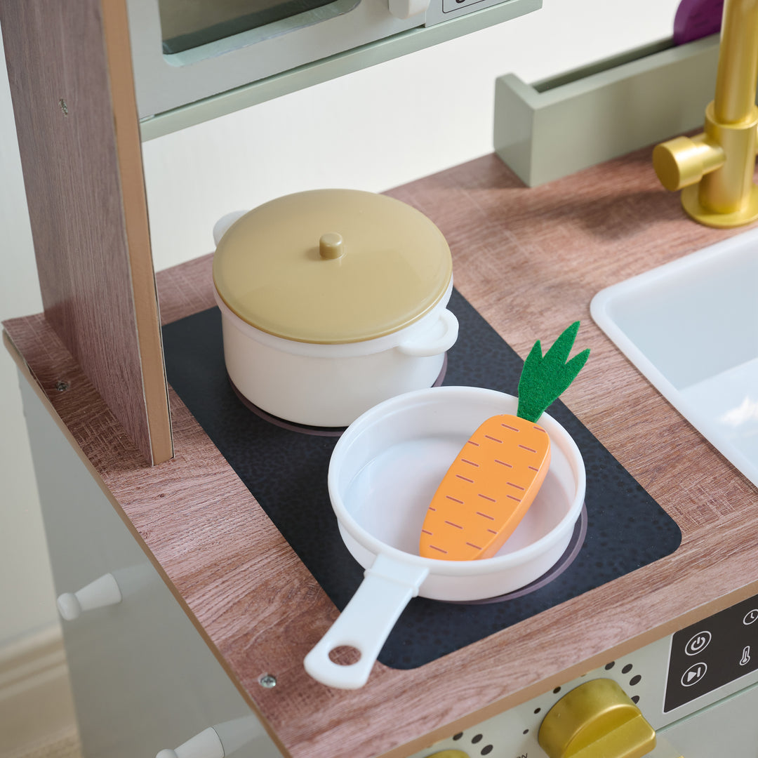 Close-up of toy stovetop with white pot and pan, featuring a wooden carrot, part of a wooden play kitchen set.