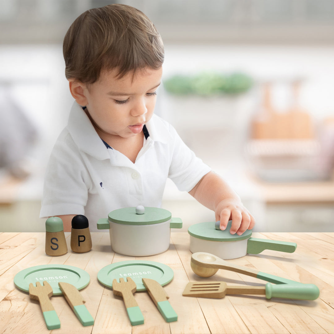 A little boy lifting the lid on a play pot in a play kitchen playset