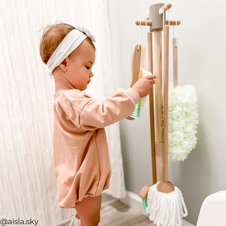 A little girl pulling on a play cleaning brush and dustpan off an organizational stand