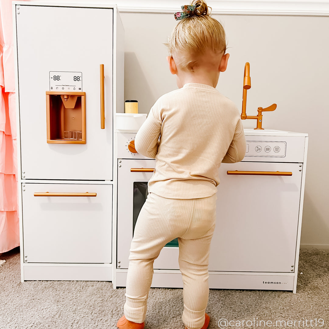 A little girl standing at a play kitchen