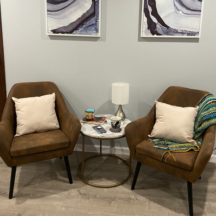 A pair of brown side accent chairs on either side of a small round faux marble table