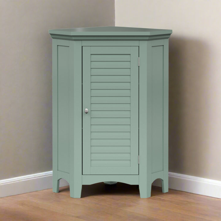 A sage green corner floor cabinet in the corner of a tan room on a hardwood floor.