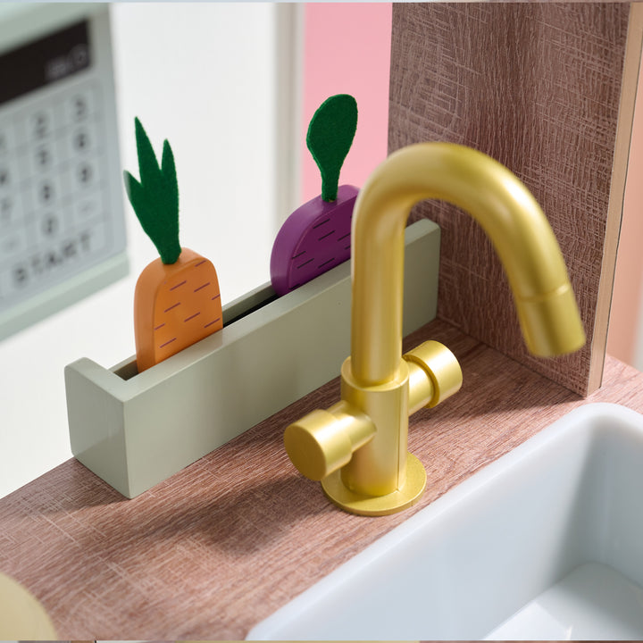 Close-up of gold toy faucet in front of a mini garden with wooden carrot and turnip, on a wooden countertop of a play kitchen