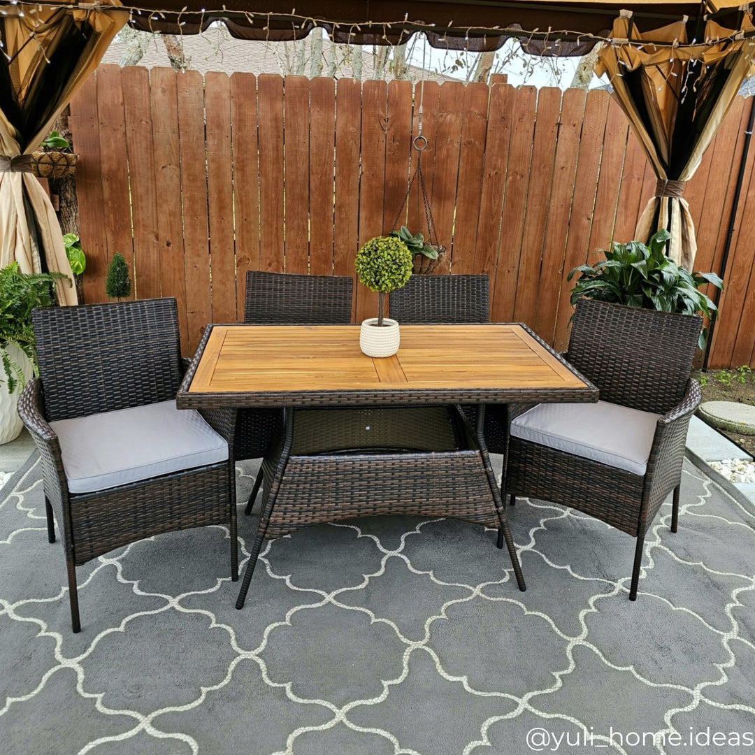 A 5-piece PE rattan dining set on an outdoor carpet underneath a pergola