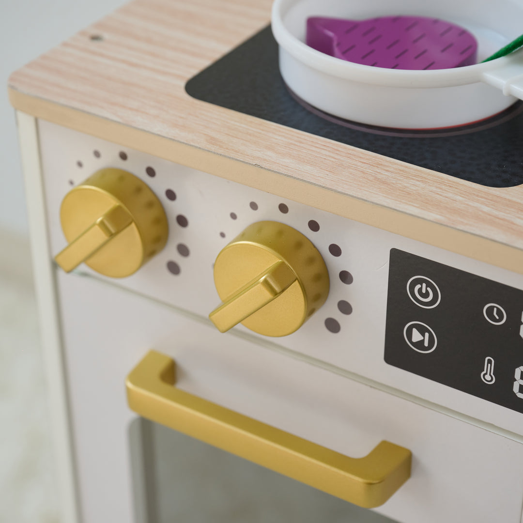 Close-up of toy stovetop with gold knobs, oven handle, and a white frying pan holding a wooden vegetable on a wooden play kitchen.
