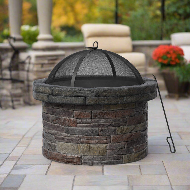 A round faux brick wood burning fire pit with a spark screen and poker on a slate patio