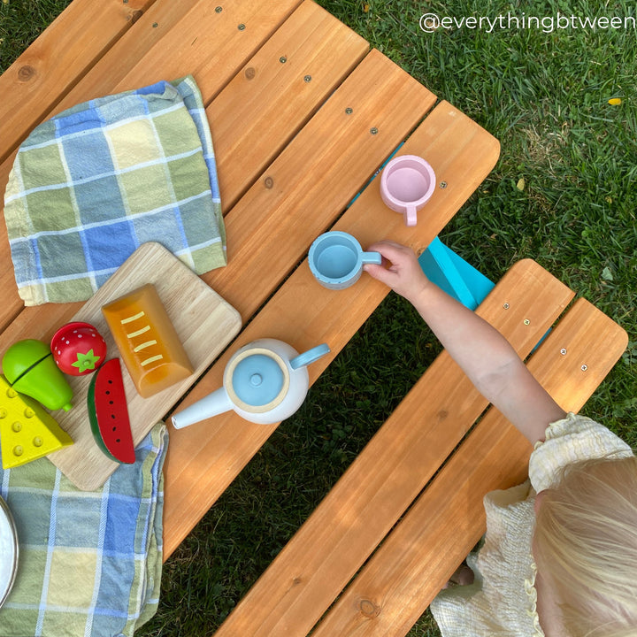 A kid playing with wooden tea cups on Teamson Kids Child Sized Wooden Outdoor Picnic Table