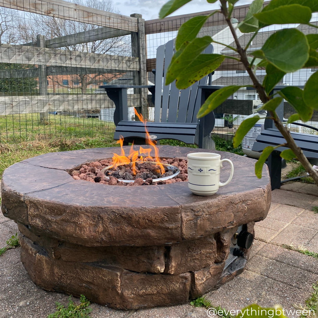 A round faux brick gas fire pit with a coffee cup on the edge