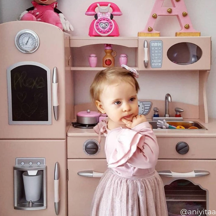 A little girl standing by a retro style pink play kitchen